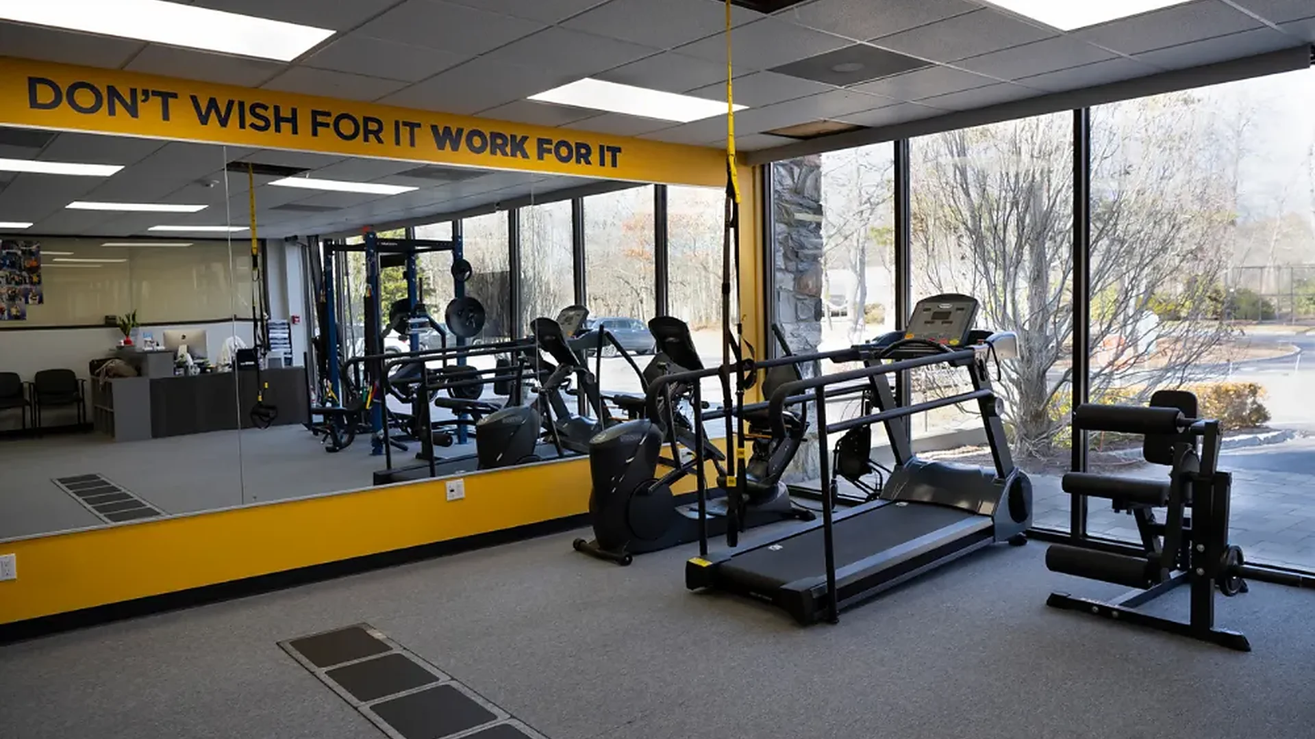 The gym floor at Greiner Physical Therapy in Speonk, NY, with treadmill, cable equipment and a mirrored wall
