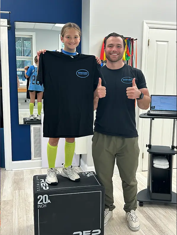 A Greiner physical therapist giving a thumbs up beside a young athlete holding up a Greiner Physical Therapy shirt