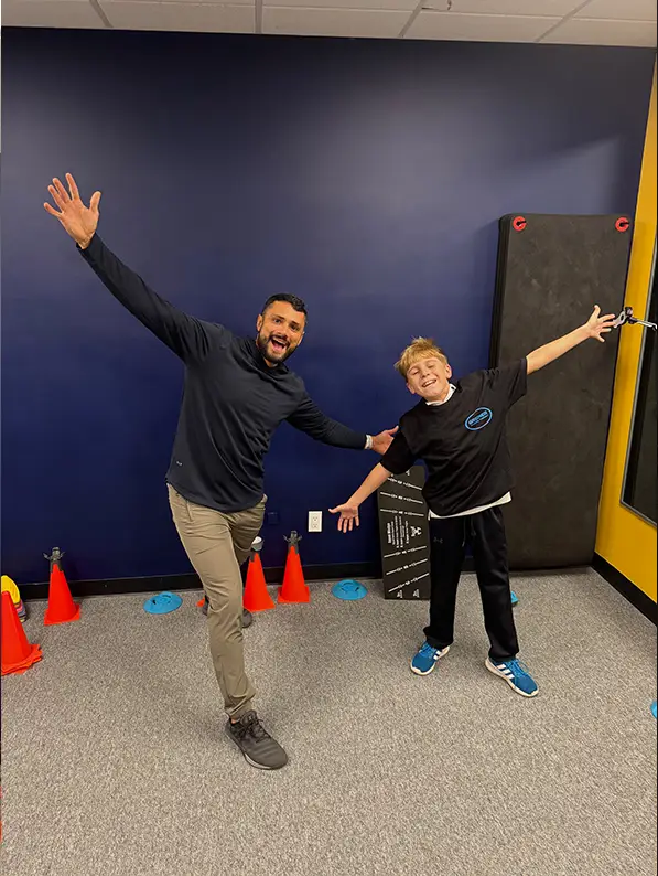 A Greiner physical therapist and a young athlete celebrating with arms outstretched in the clinic training room